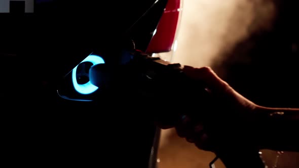 Closeup Female Hand Inserting Electric Charge in Car with Backlit Fog at Background