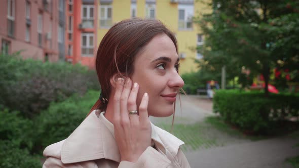Young Female Inserting Earphones in Outdoor Near Building