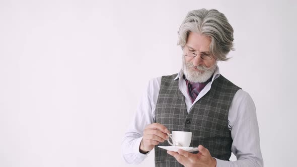 A Senior Stylih Man with a Cup of Coffee Is Standing Against White Background