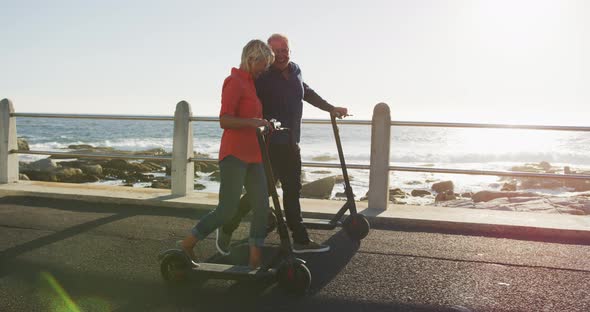 Senior couple walking next to electronic scooter alongside beach