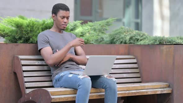 Young African Man Thinking and Using Laptop on Bench