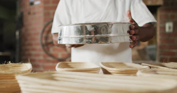 Animation of midsection of african american male baker sieving flour on board