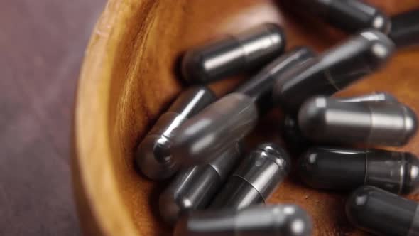 Charcoal black capsules fall into a wooden bowl in slow motion. Macro