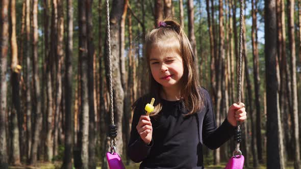 Little Girl Eats Ice Cream on a Swing in the Spring Forest