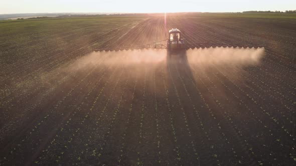 Aerial View of Farming Tractor Spraying on Field with Sprayer, Herbicides and Pesticides at Sunset