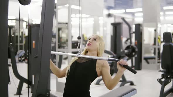 Attractive Young Blond Caucasian Woman with Sporty Body Performing Weightlifting on a Lat Pulldown