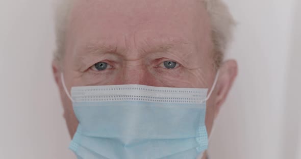 Portrait of Senior Man with Medical Mask on Face Looks Up Sadly Into Camera