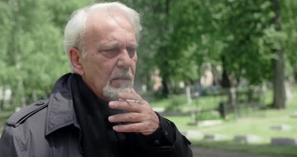 Sad Old Gray Haired Man Smokes Cigarette on the Cemetery Sorrow and Sadness About Lost of Close
