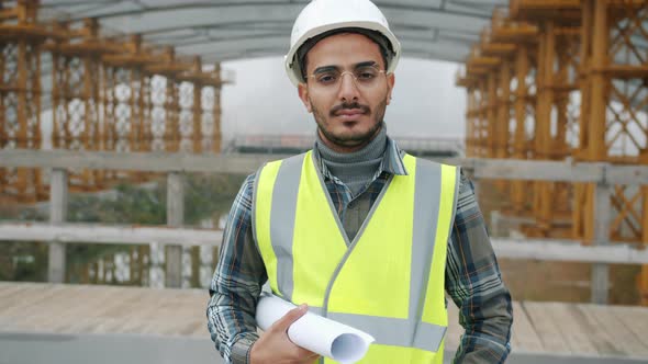 Slow Motion Portrait of Arab Construction Specialist in Helmet Standing in Building Site Holding