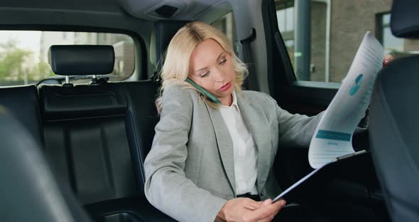 Business Woman in Glasses Sitting on Backseat of Expensive Car when Working, Talking on Phone