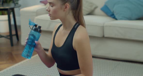 Young and Fit Woman Sitting on the Floor at Home After Intensive Sport Workout and Drinking Water