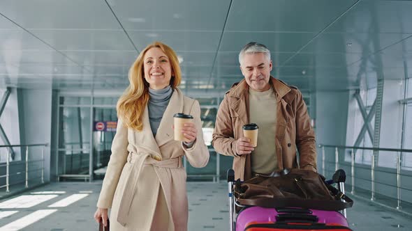 Couple of Happy Mature Travellers Enjoying Coffeetogo Going Down the Airport Terminal with Luggage