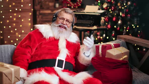 Cheerful Male Santa Claus Listening Music in Headphones Use Smartphone