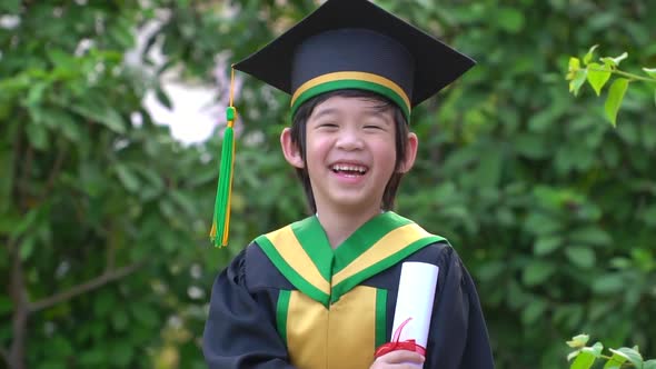 Happy Asian Child In Graduation Gowns Holding A Certificate