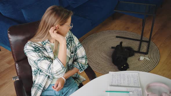 Young Woman Freelancer Working Remotely at Home Taking Break and Looking at Her Black Fluffy Cat