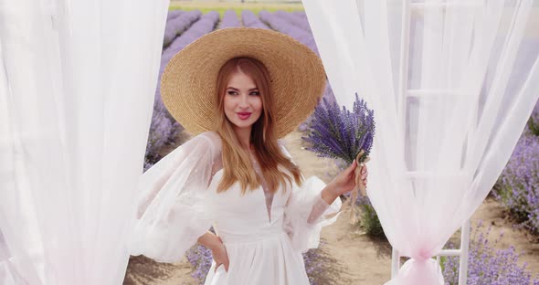 Beautiful Girl in a Hat with a Bouquet of Lavender Near the Gazebo