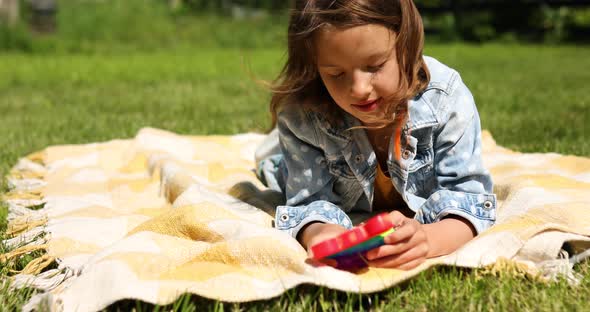 Girl Lies on a Blanket on Grass Outdoors and Play Pop It