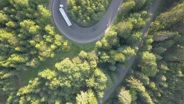 Aerial view of winding road with mowing cars and trucks in high mountain pass trough dense woods.