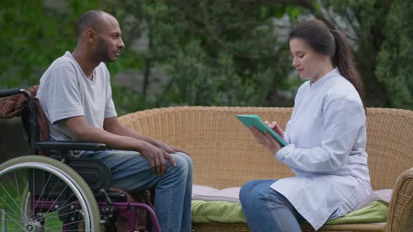 Side View of Charming Caucasian Doctor Endorsing African American Handicapped Patient in Wheelchair