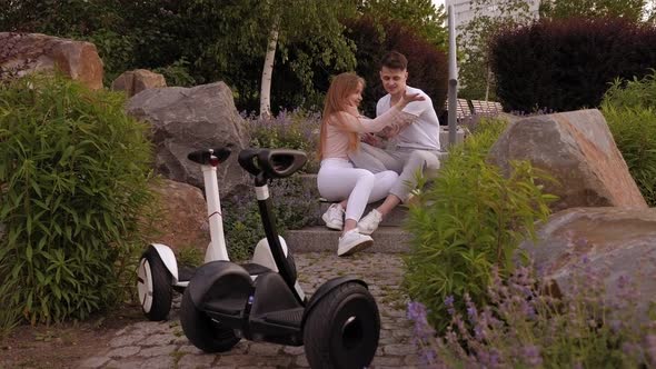 Couple Are Sitting on Stone Stairs Their Gyro Scooters Are Standing Nearby