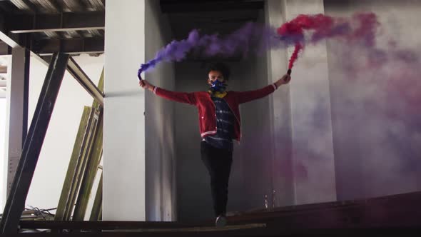 Mixed race man holding blue and purple flares walking through an empty building