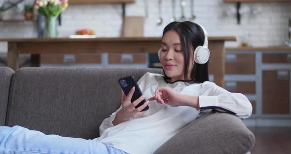 Serene Young Asian Woman Relaxing on Comfortable Sofa with Eyes Closed Wearing Headphones