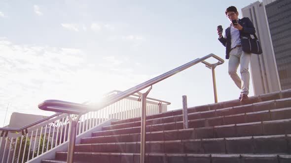 Asian man holding coffee cup using smartphone running down the stairs at corporate park