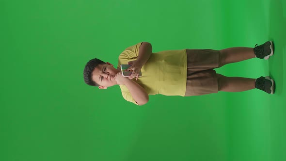 Full Body Of Asian Little Boy Use Mobile Phone And Thinking On Green Screen In The Studio