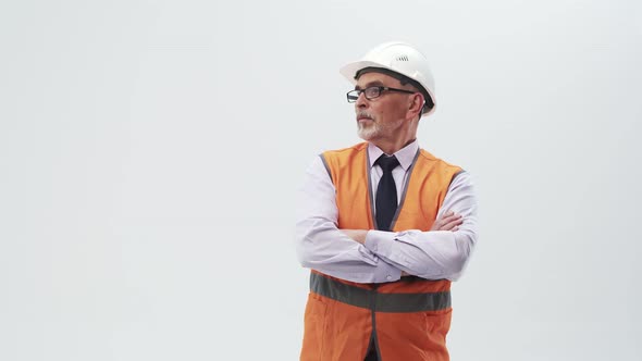 Adult man engineer in a working uniform and helmet puts hands on chest and looks to the side.