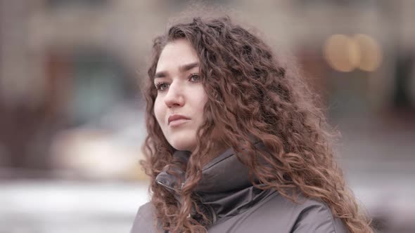 Portrait of a Young Woman with Curly Hair Posing on a City Street on a Cold Day