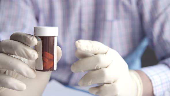 Doctor Hand in Protective Gloves Holding Pill Container