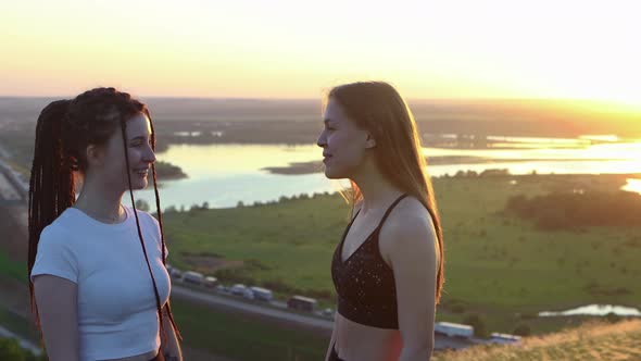 Two Young Women Talking on a Background of Sunset Field and River