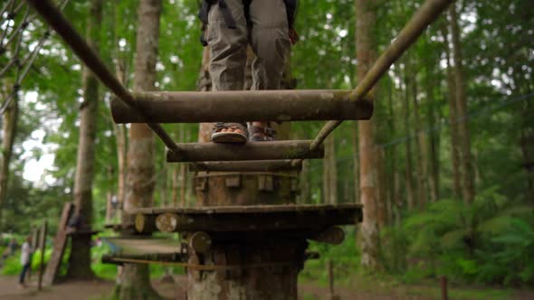 Superslowmotion Shot of a Little Boy in a Safety Harness Climbs on a Route in Treetops in a Forest