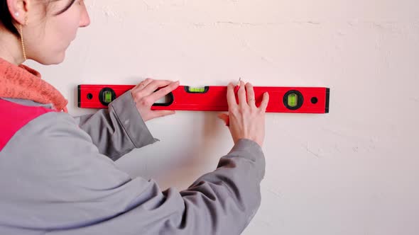 Drawing horizontal markings on the wall by level - DIY home repair. A woman in a red baseball cap an