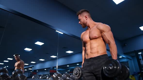 Fitness model with dumbbell. Athletic man exercising with dumbbells in the gym