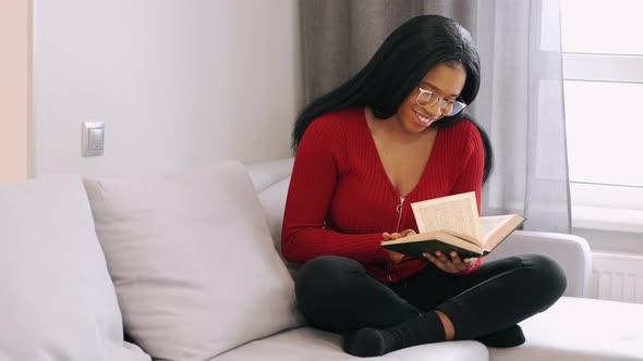 African American Woman Reading a Book Sitting on Bed at Home