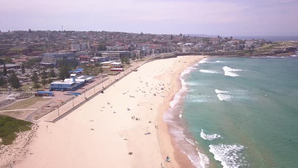 Reverse aerial flight over sandy beach at the eastern suburb Maroubra town center and blue transpare