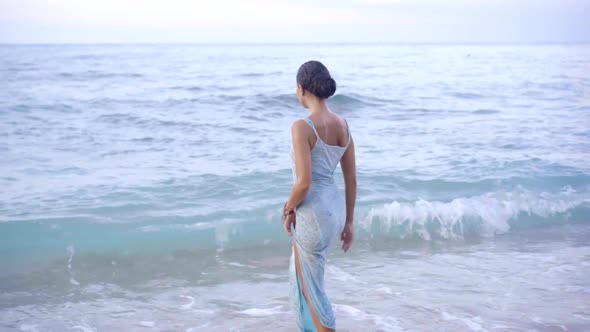 Stunning Brunette Woman in Dress Entering Ocean Wavy Water on the Island Coastline Walking on the