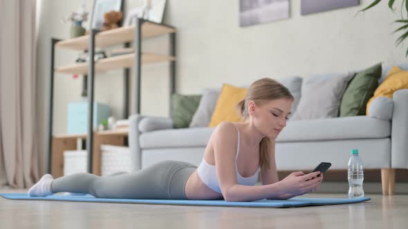 Young Woman Using Smartphone Laying on Yoga Mat