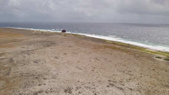 Aerial approach to the sandy shore with a rusty shipwreck on top