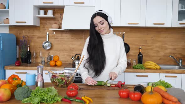 Brunette Female Cooking Healthy Food On Kitchen And Dancing In Headphones