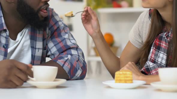 Girl Feeding African-American Boyfriend With Tasty Cake, Couple Drinking Coffee