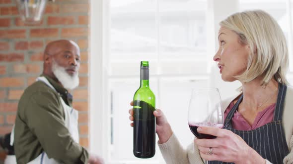 Caucasian senior woman wearing apron pouring wine into a glass in the kitchen at home