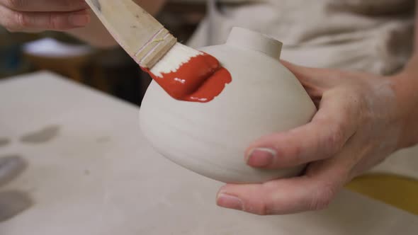 Close up view of female potter wearing apron using glaze brush to paint on pot at pottery studio