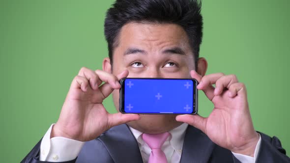 Young Handsome Overweight Asian Businessman Against Green Background