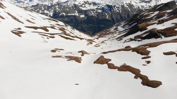 Aerial: flying over hiker walking towards snowy mountain top, ski touring mountaineering snow