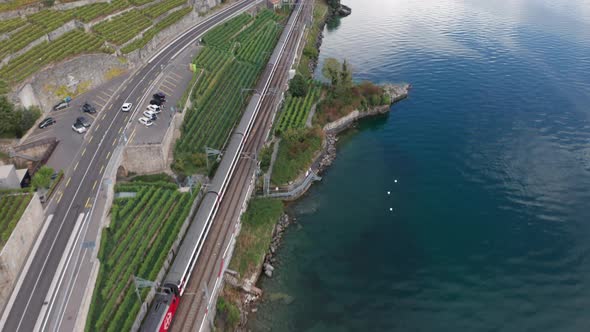 aerial of train driving through Swiss countryside, tilting up and revealing beautiful lake with dist