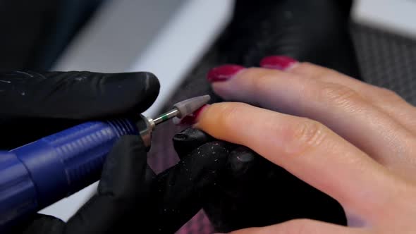 Skilled Beautician in Black Gloves Handles Red Manicure