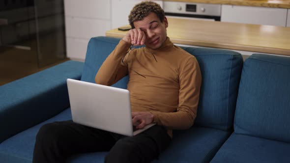 Diverse Ethnic Young Man Using Laptop on the Sofa and Got Tired