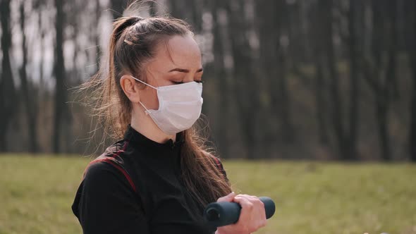 Athletic Woman in a Protective Mask Is Doing Exercise with Dumbbells